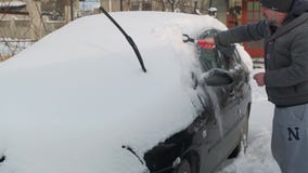 Person kehrt vom Dach eines Autos mit einem Besen den Schnee ab