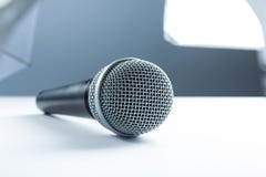Ein Mikrofon, das auf einer weißen Tabelle liegt Vor dem hintergrund der Studioausrüstung Beleuchtung stockbild Ein Mikrofon, das auf einer weißen Tabelle liegt Vor dem hintergrund der Studioausrüstung Beleuchtung stockbild