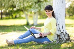 Ein Mädchen sitzt mit einem Laptop nahe einem Baum stockfoto Ein Mädchen sitzt mit einem Laptop nahe einem Baum stockfoto