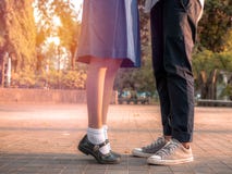 Ein Paar, das zusammen stehen, Beine und Turnschuhe von Paaren in der Schuluniform, die im Park, Symbolzeichen-Paarumfassung steh lizenzfreie stockbilder Ein Paar, das zusammen stehen, Beine und Turnschuhe von Paaren in der Schuluniform, die im Park, Symbolzeichen-Paarumfassung steh lizenzfreie stockbilder