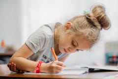 Ein siebenjähriges Mädchen sitzt zu Hause an einem Tisch und schreibt in ein Notizbuch, schließt eine Lernenaufgabe ab oder wiede stockbilder Ein siebenjähriges Mädchen sitzt zu Hause an einem Tisch und schreibt in ein Notizbuch, schließt eine Lernenaufgabe ab oder wiede stockbilder