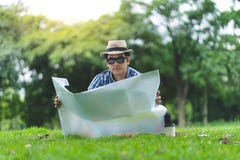 Ein älterer Mann des glücklichen Reisenden sitzen in Forrest und öffnen eine Karte lizenzfreies stockbild Ein älterer Mann des glücklichen Reisenden sitzen in Forrest und öffnen eine Karte lizenzfreies stockbild