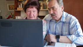 Ein älteres Paar sitzt zu Hause am Laptop Eine Frau liest Nachrichten, sitzt ein Mann mit einem Schnurrbart nahe bei ihm und spri stock video Ein älteres Paar sitzt zu Hause am Laptop Eine Frau liest Nachrichten, sitzt ein Mann mit einem Schnurrbart nahe bei ihm und spri stock video