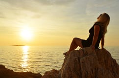 Eine Frau, die auf einer Klippe durch ihn Meer sitzt lizenzfreie stockfotos Eine Frau, die auf einer Klippe durch ihn Meer sitzt lizenzfreie stockfotos