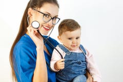 Eine junge Ärztin hält ein Baby in ihren Armen und das Baby lächelt an einem Stethoskop Weißer Hintergrund lizenzfreies stockbild Eine junge Ärztin hält ein Baby in ihren Armen und das Baby lächelt an einem Stethoskop Weißer Hintergrund lizenzfreies stockbild