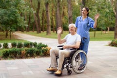 Eine Krankenschwester und ein alter Mann, der in einem Rollstuhl glücklich sitzt, grüßen jemand Stockbilder Eine Krankenschwester und ein alter Mann, der in einem Rollstuhl glücklich sitzt, grüßen jemand Stockbilder