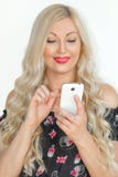 Eine schöne junge Blondine mit dem langen Haar, das auf einem Handy und einem Lächeln nett, auf einem weißen Hintergrund spielt D lizenzfreie stockbilder Eine schöne junge Blondine mit dem langen Haar, das auf einem Handy und einem Lächeln nett, auf einem weißen Hintergrund spielt D lizenzfreie stockbilder