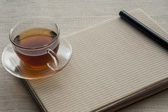 Eine Tasse Tee ist auf dem Notizbuch und dem Stift lizenzfreie stockfotos Eine Tasse Tee ist auf dem Notizbuch und dem Stift lizenzfreie stockfotos