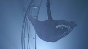 El acróbata gira en una luna de la estructura del metal en una secuencia vertical Fondo negro del humo Cámara lenta Cierre para a almacen de video El acróbata gira en una luna de la estructura del metal en una secuencia vertical Fondo negro del humo Cámara lenta Cierre para a almacen de video