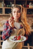 El ama de casa joven sonriente en delantal prepara la ensalada fotos de archivo libres de regalías El ama de casa joven sonriente en delantal prepara la ensalada fotos de archivo libres de regalías