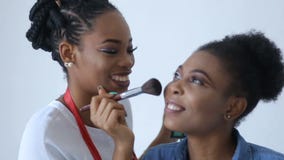 El artista de maquillaje africano feliz está aplicando el polvo en la cara del modelo africano asombroso con sonrisa bonita almacen de metraje de vídeo El artista de maquillaje africano feliz está aplicando el polvo en la cara del modelo africano asombroso con sonrisa bonita almacen de metraje de vídeo
