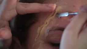 El artista de maquillaje profesional de la mujer del primer aplica la cera en cara de la muchacha linda joven para el maquillaje almacen de video El artista de maquillaje profesional de la mujer del primer aplica la cera en cara de la muchacha linda joven para el maquillaje almacen de video