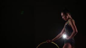 El atleta atractivo delgado de la muchacha de la vista lateral en traje de baño colorido brillante en gimnasia rítmica se coloca El atleta atractivo delgado de la muchacha de la vista lateral en traje de baño colorido brillante en gimnasia rítmica se coloca