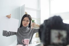 El blogger femenino enojado se está sentando en la tabla y el vídeo de registración Ella está mirando al papel que ella se está s imágenes de archivo libres de regalías El blogger femenino enojado se está sentando en la tabla y el vídeo de registración Ella está mirando al papel que ella se está s imágenes de archivo libres de regalías