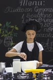 El cocinero bonito de la muchacha en un delantal negro y un sombrero del ` s del cocinero revuelve con el SP imagen de archivo libre de regalías El cocinero bonito de la muchacha en un delantal negro y un sombrero del ` s del cocinero revuelve con el SP imagen de archivo libre de regalías