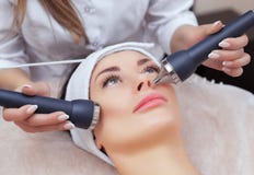 El cosmetologist hace el procedimiento una limpieza ultrasónica de la piel facial de una mujer hermosa, joven en un salón de bell fotografía de archivo El cosmetologist hace el procedimiento una limpieza ultrasónica de la piel facial de una mujer hermosa, joven en un salón de bell fotografía de archivo