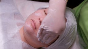 El cosmetólogo profesional en los guantes blancos pone una crema de alimentación en la cara de una mujer asiática Procedimiento c almacen de metraje de vídeo El cosmetólogo profesional en los guantes blancos pone una crema de alimentación en la cara de una mujer asiática Procedimiento c almacen de metraje de vídeo