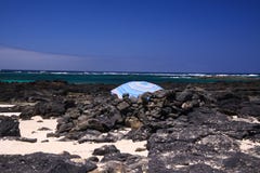El Cotillo - Faro del Toston: Isolated blue umbrella between black volcanic rocks on beach with ocean horizon north Fuerteventura stock photo El Cotillo - Faro del Toston: Isolated blue umbrella between black volcanic rocks on beach with ocean horizon north Fuerteventura stock photo