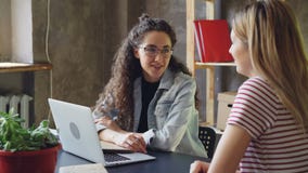 El dueño joven de la pequeña empresa está hablando con su cliente en oficina moderna Las mujeres se están sentando en el escritor metrajes El dueño joven de la pequeña empresa está hablando con su cliente en oficina moderna Las mujeres se están sentando en el escritor metrajes