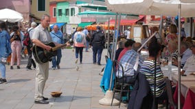 El ejecutante de la calle recoge el dinero tocando la guitarra en el cuadrado con la gente El ejecutante de la calle recoge el dinero tocando la guitarra en el cuadrado con la gente