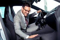 El hombre de negocios hermoso se está sentando en un nuevo coche en concesión de coche imágenes de archivo libres de regalías El hombre de negocios hermoso se está sentando en un nuevo coche en concesión de coche imágenes de archivo libres de regalías