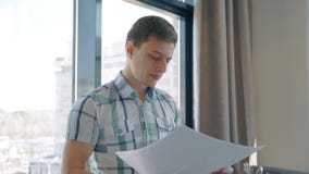 El hombre de negocios joven está trabajando con la ventana que hace una pausa del proyecto en interior moderno almacen de video El hombre de negocios joven está trabajando con la ventana que hace una pausa del proyecto en interior moderno almacen de video