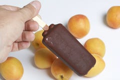 El hombre está sosteniendo el helado de chocolate en sus manos Contra la perspectiva de los albaricoques dispersados en la tabla Fotografía de archivo libre de regalías El hombre está sosteniendo el helado de chocolate en sus manos Contra la perspectiva de los albaricoques dispersados en la tabla Fotografía de archivo libre de regalías