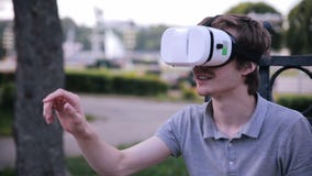El hombre hermoso joven que lleva las gafas de la realidad virtual que se sientan en una ciudad parquea metrajes El hombre hermoso joven que lleva las gafas de la realidad virtual que se sientan en una ciudad parquea metrajes