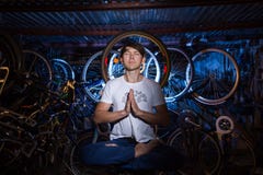 El hombre joven está practicando yoga en garaje con muchas bicicletas detrás Fotos de archivo El hombre joven está practicando yoga en garaje con muchas bicicletas detrás Fotos de archivo