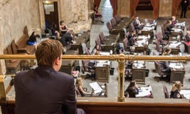 El hombre joven se sienta en galería y mira procedimientos legislativos fotos de archivo El hombre joven se sienta en galería y mira procedimientos legislativos fotos de archivo
