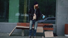 El hombre sin hogar muy borracho con la muestra de la cartulina y del alcohol pide dinero mientras que coloca el banco cercano en foto de archivo libre de regalías El hombre sin hogar muy borracho con la muestra de la cartulina y del alcohol pide dinero mientras que coloca el banco cercano en foto de archivo libre de regalías
