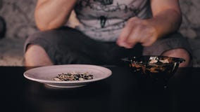 El hombre toma las semillas de la situación de la taza en la tabla y las limpia de la cáscara El hombre lanza la cáscara en una p metrajes El hombre toma las semillas de la situación de la taza en la tabla y las limpia de la cáscara El hombre lanza la cáscara en una p metrajes