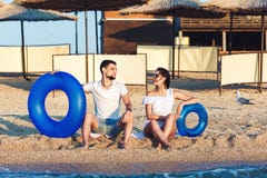 El hombre y la mujer se están sentando en la playa y están llevando a cabo círculos inflables concepto de día de fiesta del mar d foto de archivo libre de regalías El hombre y la mujer se están sentando en la playa y están llevando a cabo círculos inflables concepto de día de fiesta del mar d foto de archivo libre de regalías