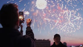 El individuo joven está sosteniendo un smartphone con la luz chispeante y está registrando un vídeo de fuegos artificiales en el metrajes El individuo joven está sosteniendo un smartphone con la luz chispeante y está registrando un vídeo de fuegos artificiales en el metrajes