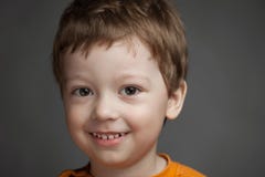 El muchacho con emociones positivas en un fondo gris, niño sonríe ch Imagen de archivo El muchacho con emociones positivas en un fondo gris, niño sonríe ch Imagen de archivo