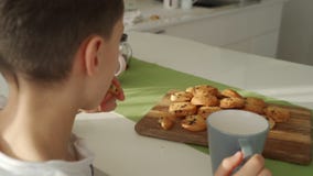 El muchacho desayuna en cocina moderna El muchacho come la galleta con leche Tabla blanca en cocina Gray Bowl en la tabla Cierre almacen de metraje de vídeo El muchacho desayuna en cocina moderna El muchacho come la galleta con leche Tabla blanca en cocina Gray Bowl en la tabla Cierre almacen de metraje de vídeo