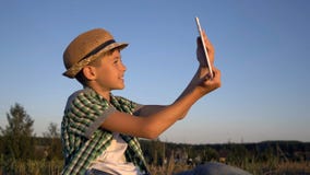 El muchacho en un sombrero se sienta en el top y las negociaciones sobre la comunicación video usando una tableta imagen de archivo El muchacho en un sombrero se sienta en el top y las negociaciones sobre la comunicación video usando una tableta imagen de archivo