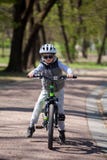 El ni?o peque?o aprende montar una bici en el parque El muchacho lindo en gafas de sol monta una bici Ni?o sonriente feliz en el imagen de archivo libre de regalías El ni?o peque?o aprende montar una bici en el parque El muchacho lindo en gafas de sol monta una bici Ni?o sonriente feliz en el imagen de archivo libre de regalías