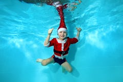 El niño en un casquillo y vestido como Santa Claus nada y presenta bajo el agua en un fondo azul, mirando la cámara y la sonrisa fotos de archivo El niño en un casquillo y vestido como Santa Claus nada y presenta bajo el agua en un fondo azul, mirando la cámara y la sonrisa fotos de archivo