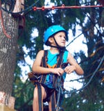 El niño pequeño en un casco protector y en el equipo especial pasa una carrera de obstáculos en la altura foto de archivo libre de regalías El niño pequeño en un casco protector y en el equipo especial pasa una carrera de obstáculos en la altura foto de archivo libre de regalías