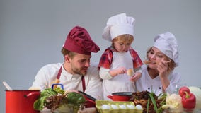 El niño pequeño lindo y sus padres hermosos están sonriendo mientras que cocina en cocina Familia joven que cocina la comida en c almacen de video El niño pequeño lindo y sus padres hermosos están sonriendo mientras que cocina en cocina Familia joven que cocina la comida en c almacen de video