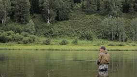 El pescador alegre está pescando en agua de río tranquila cerca de la orilla almacen de video El pescador alegre está pescando en agua de río tranquila cerca de la orilla almacen de video