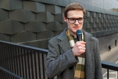 El reportero profesional de las noticias en lentes con el micrófono está difundiendo en la calle Noticias de la moda o de negocio imagen de archivo libre de regalías El reportero profesional de las noticias en lentes con el micrófono está difundiendo en la calle Noticias de la moda o de negocio imagen de archivo libre de regalías
