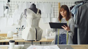 El sastre hermoso está dando vuelta a adaptación simulado para comprobar la ropa fijada y a trabajo con la tableta para incorpora metrajes El sastre hermoso está dando vuelta a adaptación simulado para comprobar la ropa fijada y a trabajo con la tableta para incorpora metrajes