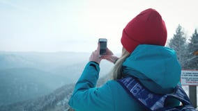 El turista de la chica joven hace la foto en smartphone en invierno Fotografía las montañas coronadas de nieve almacen de metraje de vídeo El turista de la chica joven hace la foto en smartphone en invierno Fotografía las montañas coronadas de nieve almacen de metraje de vídeo