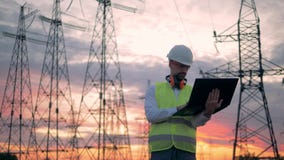 El técnico de sexo masculino está actuando un ordenador portátil al lado de líneas de transmisión eléctricas almacen de video El técnico de sexo masculino está actuando un ordenador portátil al lado de líneas de transmisión eléctricas almacen de video