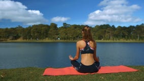 El viento sacude la cola de caballo de la muchacha en actitud de la yoga por el río El viento sacude la cola de caballo de la muchacha en actitud de la yoga por el río