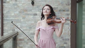 El violinista de sexo femenino confiado camina en vestido de noche que sopla, y juegos en el violín almacen de video El violinista de sexo femenino confiado camina en vestido de noche que sopla, y juegos en el violín almacen de video