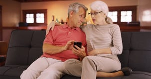 Elderly couple sitting on couch using smartphone Royalty Free Stock Images Elderly couple sitting on couch using smartphone Royalty Free Stock Images