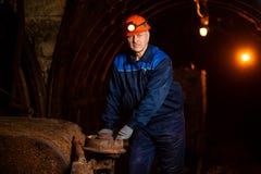 An elderly man dressed in work overalls and a helmet stands near the old inverted vogonetki. Miner stock photo An elderly man dressed in work overalls and a helmet stands near the old inverted vogonetki. Miner stock photo